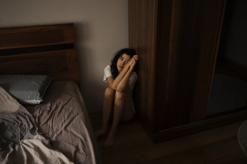 Mujer joven con ansiedad sentada en el suelo junto a su cama